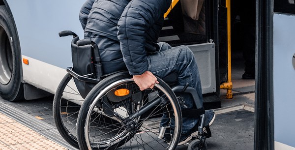 A man pushing the wheels of his wheelchair into a community vehicle. 