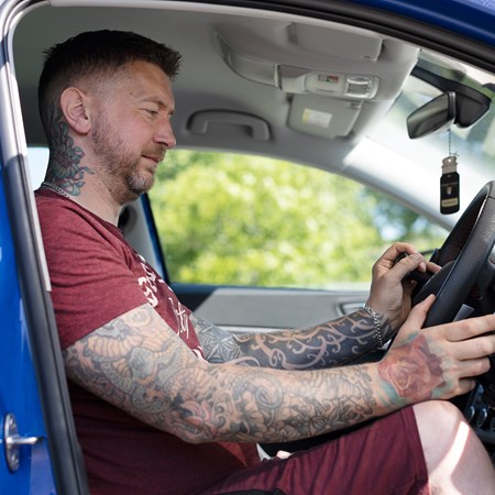 A man sitting in the driver's seat of a car holds hand controls