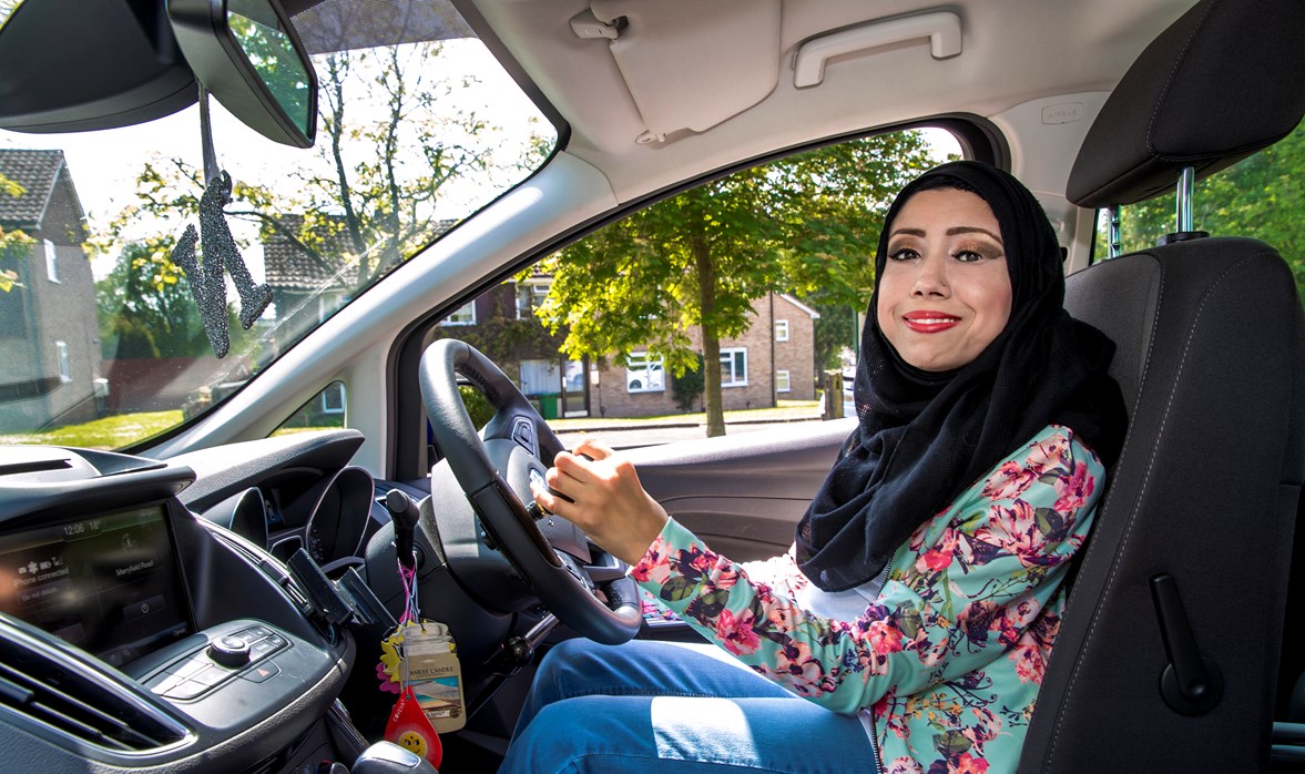 Nazmin is sat in the driving seat of her car with her hands on the specially adapted steering wheel    