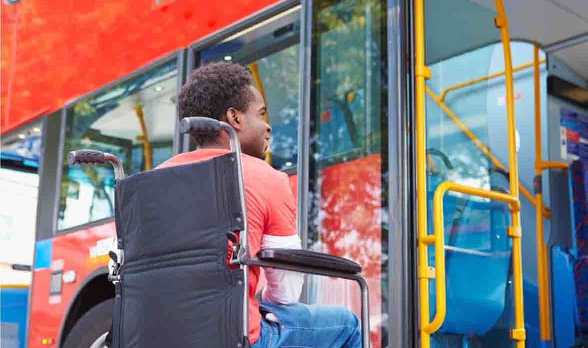 A man is sitting in a wheelchair in front of a bus. 