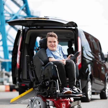 A boy in a wheelchair is next to a car. 