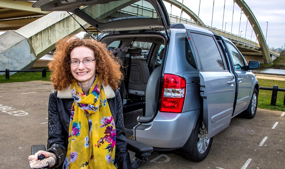 Hannah has fantastic curly hair and looks really happy as she sits outside the open boot of her adapted vehicle