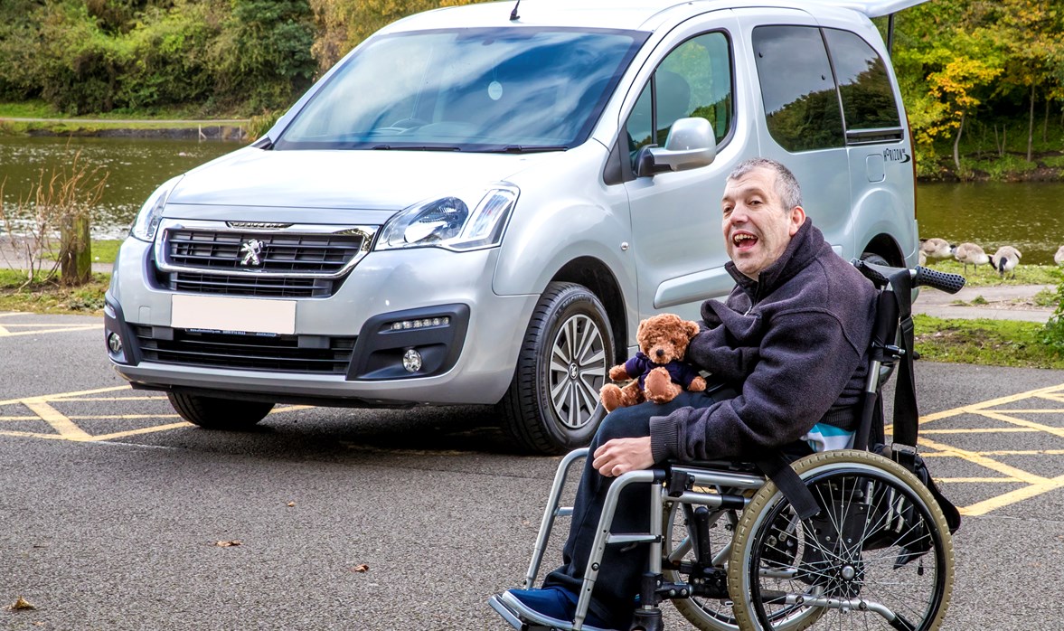 Kevin's WAV is by a river while he sits outside it, in his wheelchair, with a Motability teddy bear on his lap