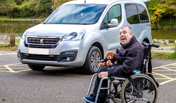 Kevin's WAV is by a river while he sits outside it, in his wheelchair, with a Motability teddy bear on his lap