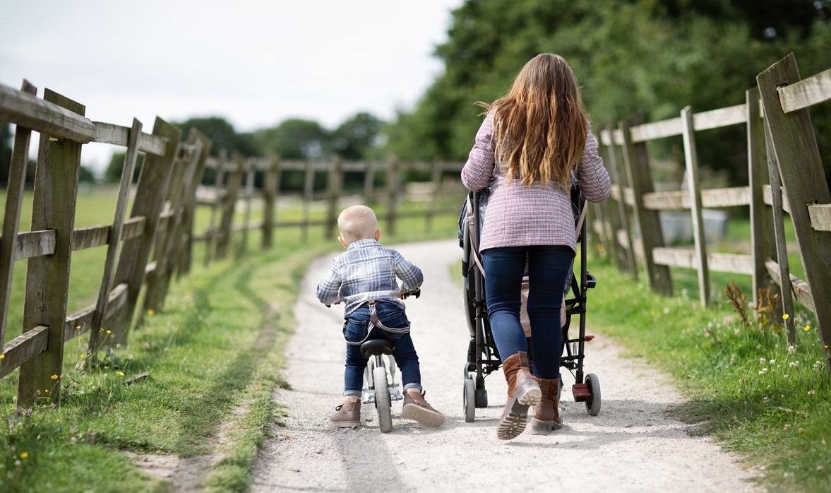 Danielle is walking down a country lane, pushing her daughter in her pushchair and her son scooting along on his bike